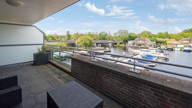 A balcony with a view of a river, boats, and houses across the water. - Spacious and luxurious apartment - Kaag Resort (26) (Warmond)