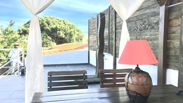 A wooden table with a red lamp and a decorative vase, set against a backdrop of a wooden wall and a view of a green landscape.