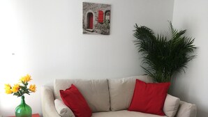 A beige sofa with red cushions, a small red table with a green vase and yellow flowers, and a large green plant.