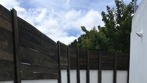 A courtyard with a wooden fence, two dark wooden planters with plants, and a set of concrete stairs leading to an upper level.