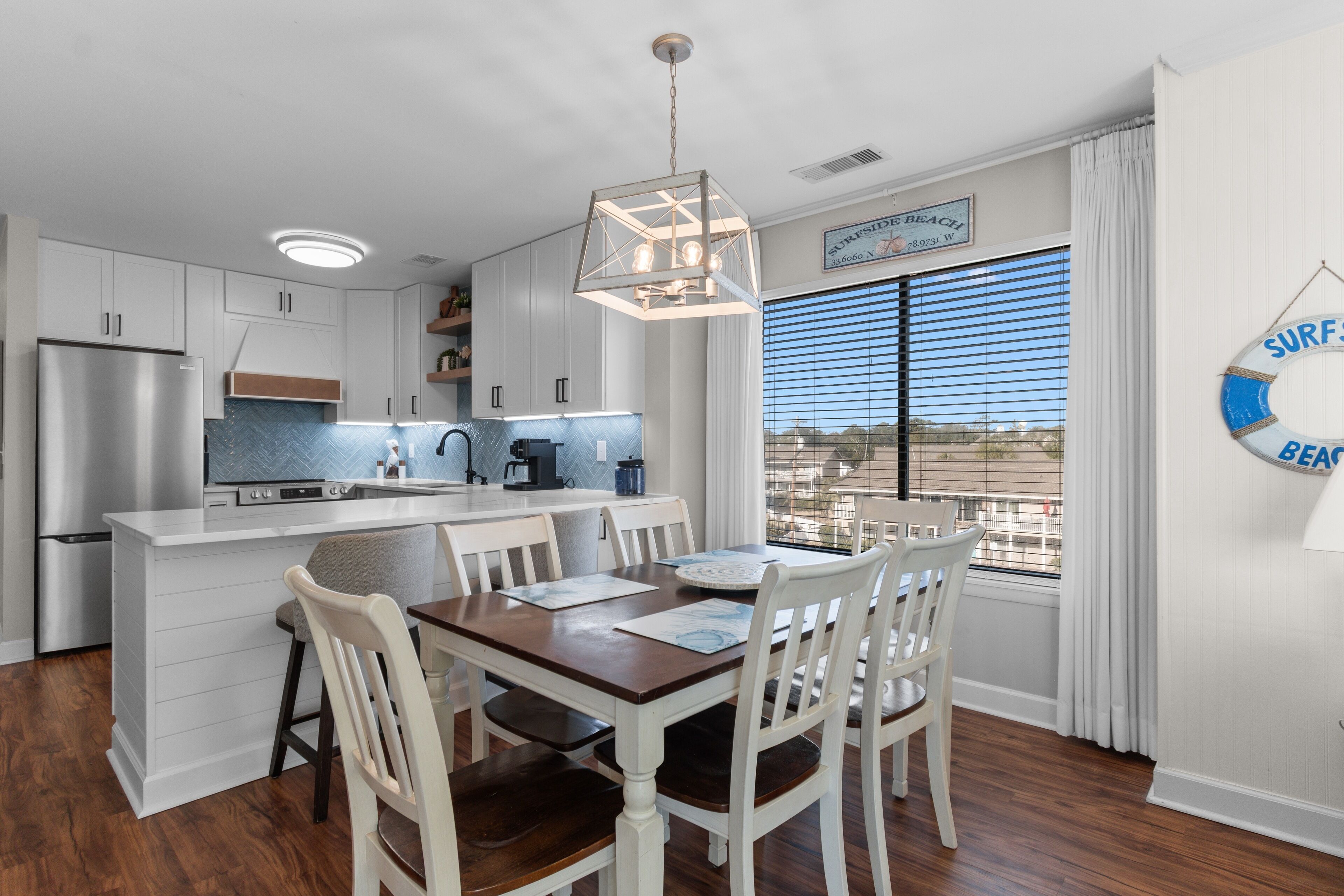 A modern kitchen with white cabinets, a stainless steel refrigerator, and a wooden dining table with chairs.
