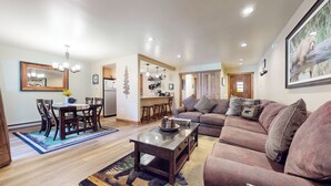 Ein geräumiges Wohnzimmer mit einer großen Couch, einem Essbereich mit Holzsesseln und einer Küchenzeile inklusive Kühlschrank und Herd.