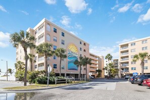 Ein mehrgeschossiges Hotel mit einem Wandbild im Strandhausstil, Palmen und einem Parkplatz.