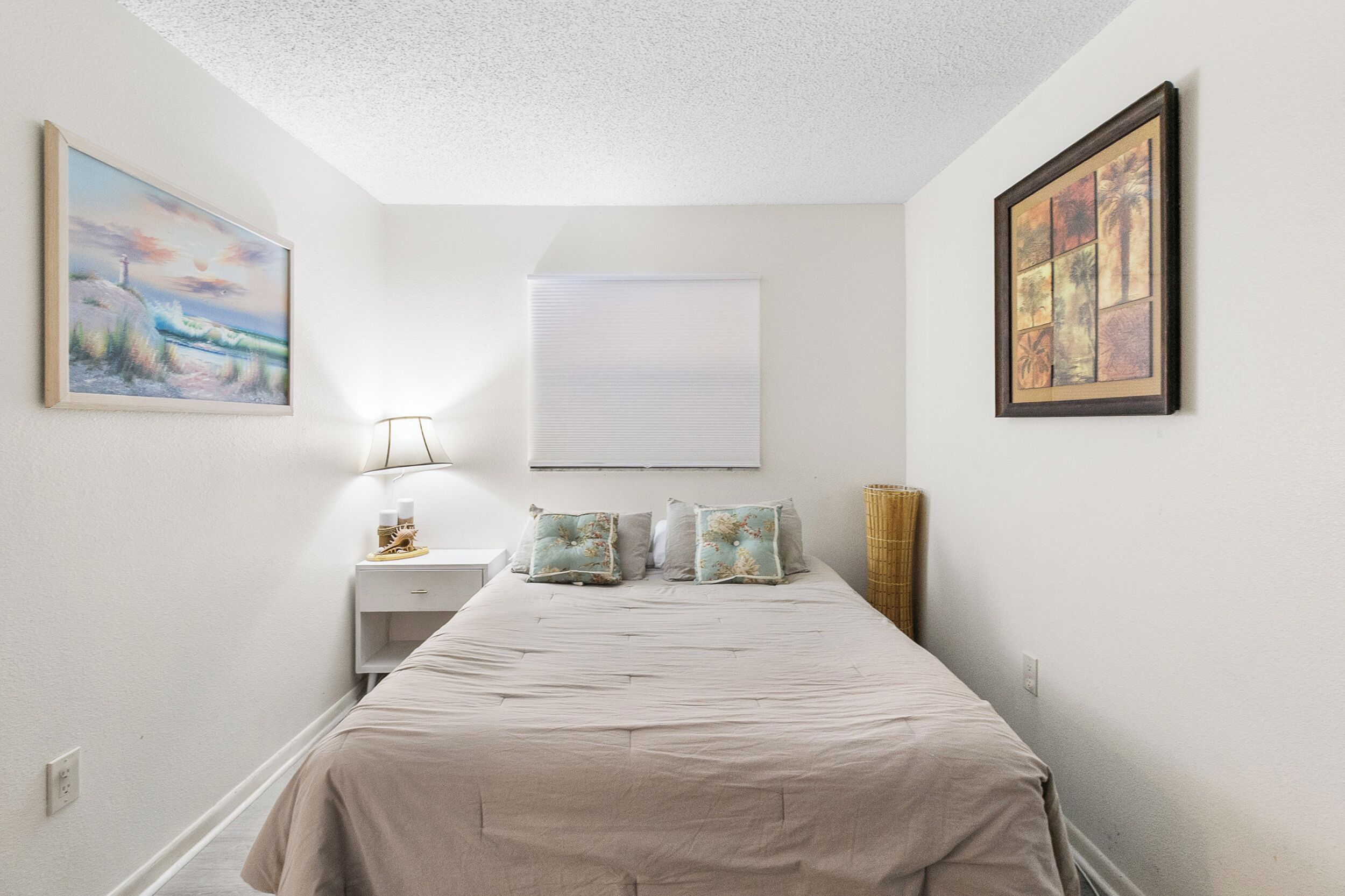 A bedroom with a bed, a nightstand, a lamp, and two framed pictures on the walls.