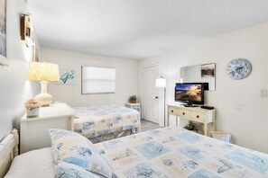 Ein Hotelzimmer mit zwei Betten, einem Fernseher, einem Schreibtisch mit Lampe und einer Wanduhr.
