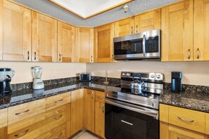 Una cocina con armarios de madera, un microondas de acero inoxidable, una estufa y una licuadora.