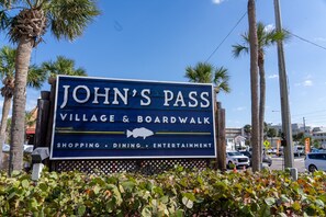 Schild für John's Pass Village & Boardwalk, das Geschäfte, Gastronomie und Unterhaltung hervorhebt.