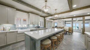 A spacious kitchen with a large island, bar stools, and a view to the living area. - Remodeled 5BR Beachfront Home w/ new main floor deck, Private Beach, Communal Pool & Bunks (Santa Rosa Beach)