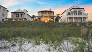 A beachfront property with a central building featuring a balcony and multiple windows, surrounded by sand and vegetation. - Remodeled 5BR Beachfront Home w/ new main floor deck, Private Beach, Communal Pool & Bunks (Santa Rosa Beach)