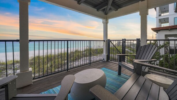 A covered outdoor area with a view of the beach, featuring a wooden deck, Adirondack chairs, and a round table. - Remodeled 5BR Beachfront Home w/ new main floor deck, Private Beach, Communal Pool & Bunks (Santa Rosa Beach)