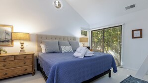 A bedroom with a large bed, a nightstand, a dresser, and a window with blinds. - 12 Dewberry: Elegant Greenwood Forest Home, Sleeps 8,Free Bikes, Pool, Tennis (Hilton Head Island)