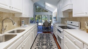 A modern kitchen with white cabinetry, stainless steel sinks, and a large window overlooking a patio. - 12 Dewberry: Elegant Greenwood Forest Home, Sleeps 8,Free Bikes, Pool, Tennis (Hilton Head Island)