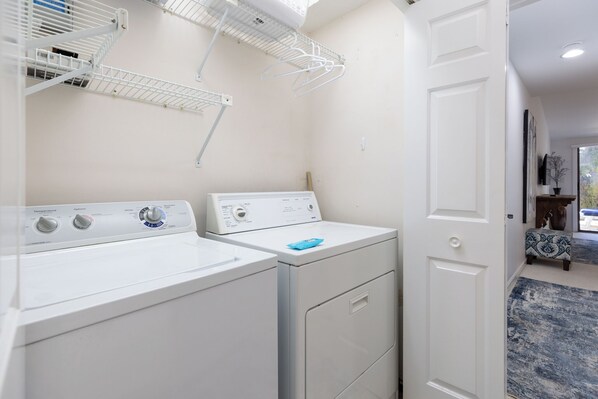 A laundry room with two white washing machines, a drying rack, and a door leading to another room.