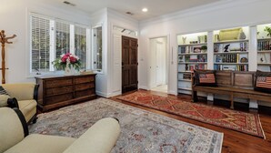 A spacious living room with a large window, a wooden bench, a bookshelf, and a decorative rug. - 12 Dewberry: Elegant Greenwood Forest Home, Sleeps 8,Free Bikes, Pool, Tennis (Hilton Head Island)