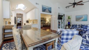 Een ruime woonkamer met een houten eettafel, blauw-wit geruit banken en een plafondventilator.