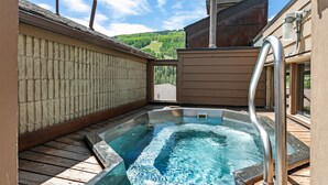 A hot tub with a wooden deck and a view of green hills in the background. - Heart of Lionshead + Free Parking - Rooftop Hot Tub (Vail)
