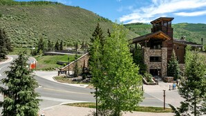 A lodge with a stone facade, a wooden tower, and a paved driveway leading to a parking area. - Heart of Lionshead + Free Parking - Rooftop Hot Tub (Vail)