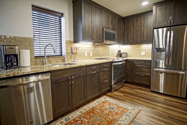 A modern kitchen with dark wood cabinets, stainless steel appliances, a built-in microwave, and a large refrigerator.
