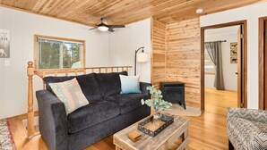 Une pièce chaleureuse avec un canapé sombre, une table basse en bois, une cheminée et un ventilateur de plafond.