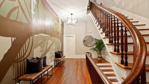 A grand staircase with a wooden handrail and a wall-mounted mirror. - Restored 1800's Condo | Downtown Savannah (Savannah)
