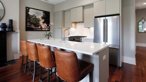 A modern kitchen with a central island, stainless steel appliances, and leather bar stools. - Restored 1800's Condo | Downtown Savannah (Savannah)