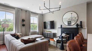 A modern living room with a sectional sofa, a fireplace, a flat-screen TV, and large windows. - Restored 1800's Condo | Downtown Savannah (Savannah)