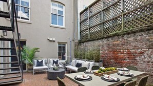 A patio with a dining table set for four, surrounded by wicker chairs and a cushioned sofa. - Restored 1800's Condo | Downtown Savannah (Savannah)