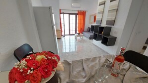Un salon comprenant un canapé, une table basse, un fauteuil, un vase décoratif avec des roses rouges et une bouteille de vin.