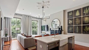 A modern kitchen with a central island, a dining area with a sofa, and a large window with curtains. - 3BR Condo | Historic Savannah District (Savannah)