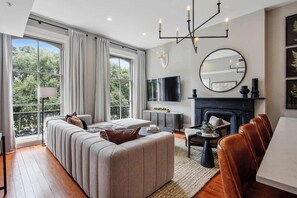 Una sala de estar moderna con sofá, chimenea, mesa de comedor y un amplio ventanal con cortinas.