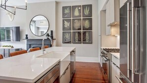A modern kitchen with a central island, stainless steel appliances, and framed botanical prints on the wall. - 3BR Condo | Historic Savannah District (Savannah)
