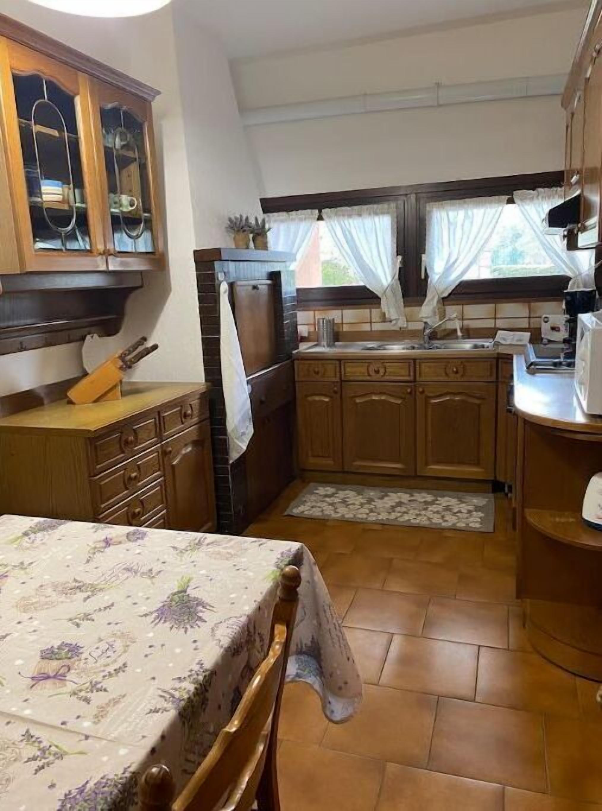 A kitchen with wooden cabinets, a tiled backsplash, a sink, and a dining table with a floral tablecloth.