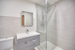 Une salle de bain moderne avec une douche à parois de verre, un meuble-lavabo blanc avec un miroir et un sol carrelé.