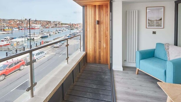 Un balcon donnant sur une marina, un canapé bleu et un mur en bois.