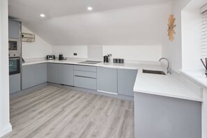A modern kitchen with grey cabinets, a white countertop, and a wooden floor.