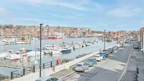 Un port de plaisance avec des bateaux amarrés, une route qui le longe et des bâtiments en arrière-plan.