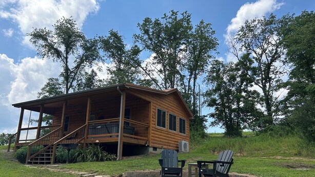 A wooden cabin with a porch, a stone fire pit, and Adirondack chairs. - A cozy new cabin in rural setting with a hot tub on porch. Beautiful rural view. (Albany)