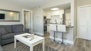 A modern apartment with a grey sofa, a white coffee table, a kitchen with white cabinets, a fridge, and a bar area with two white stools. - Siesta Key Village -Suite #2: A Block to the Beach, In the HEART of the Village! (Sarasota)