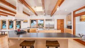 Een moderne keuken met een groot eiland, houten balken en grote ramen.