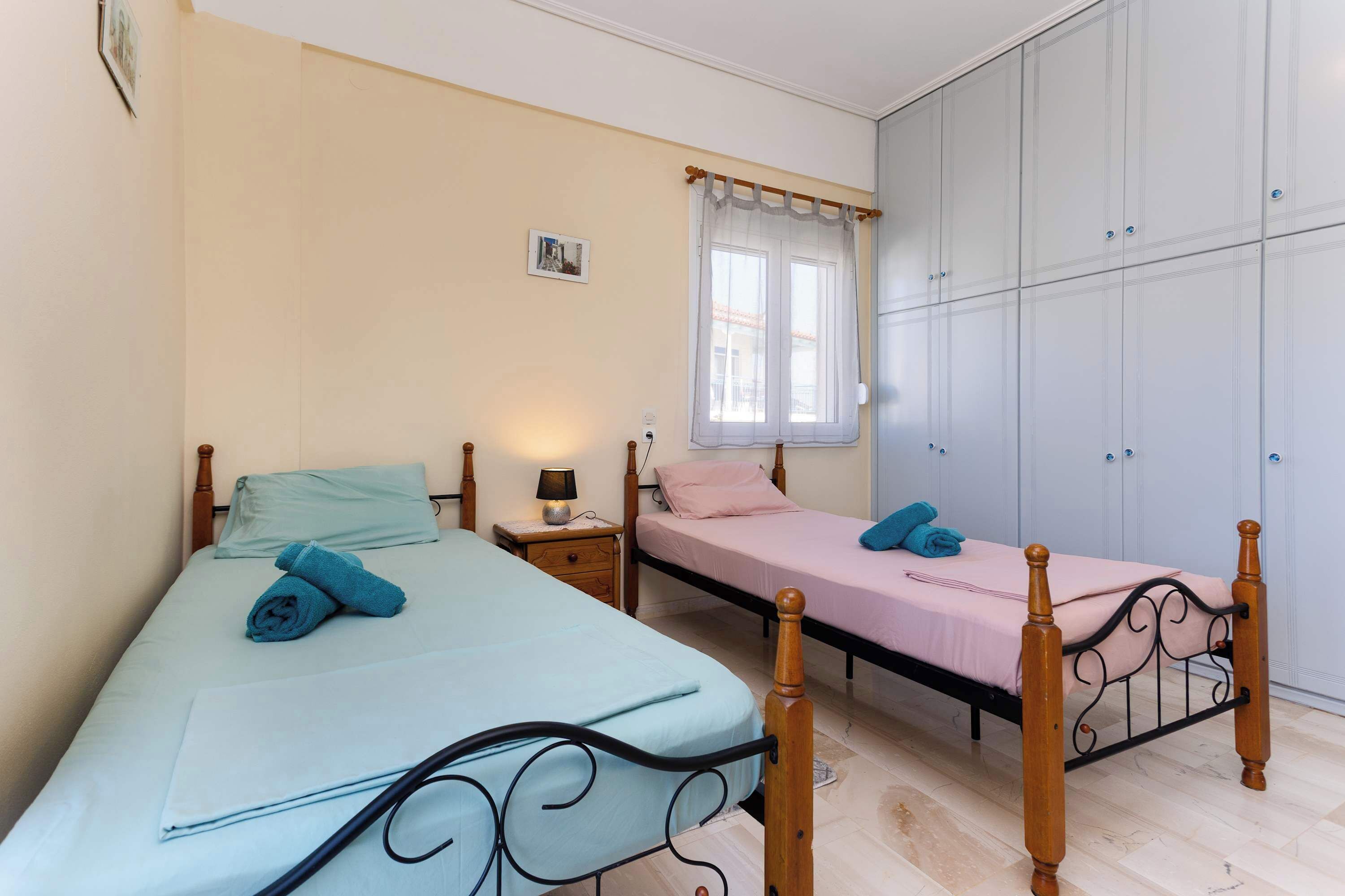 Ein Schlafzimmer mit zwei Betten, einem Kleiderschrank, einem Fenster mit Vorhängen und einem Nachttisch mit Lampe.