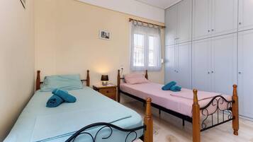 Ein Schlafzimmer mit zwei Betten, einem Kleiderschrank, einem Fenster mit Vorhängen und einem Nachttisch mit Lampe.