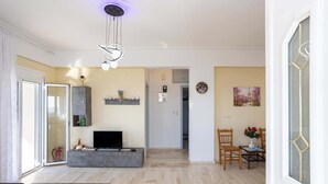 Una sala de estar moderna con un sofá gris, un televisor de pantalla plana y una zona de comedor con sillas de madera y una mesita.