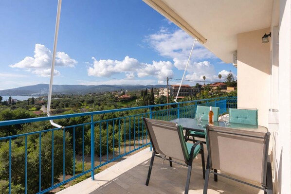 A balcony with a table and chairs, overlooking a scenic landscape with trees and buildings. - Koroni Seaview Retreat - Summer Romantic Escape (Koroni)