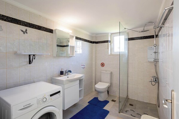 Un baño equipado con lavadora, lavamanos, inodoro y cabina de ducha de vidrio.