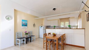 A compact kitchen with a dining area, featuring a small table and chairs, a refrigerator, and a clock on the wall. - Koroni Seaview Retreat - Summer Romantic Escape (Koroni)