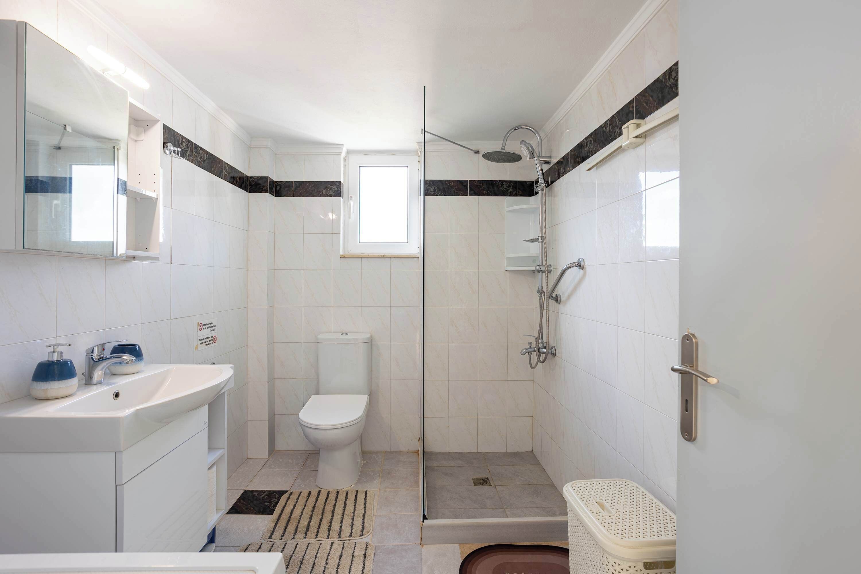 A bathroom with a toilet, sink, shower, and a small window.