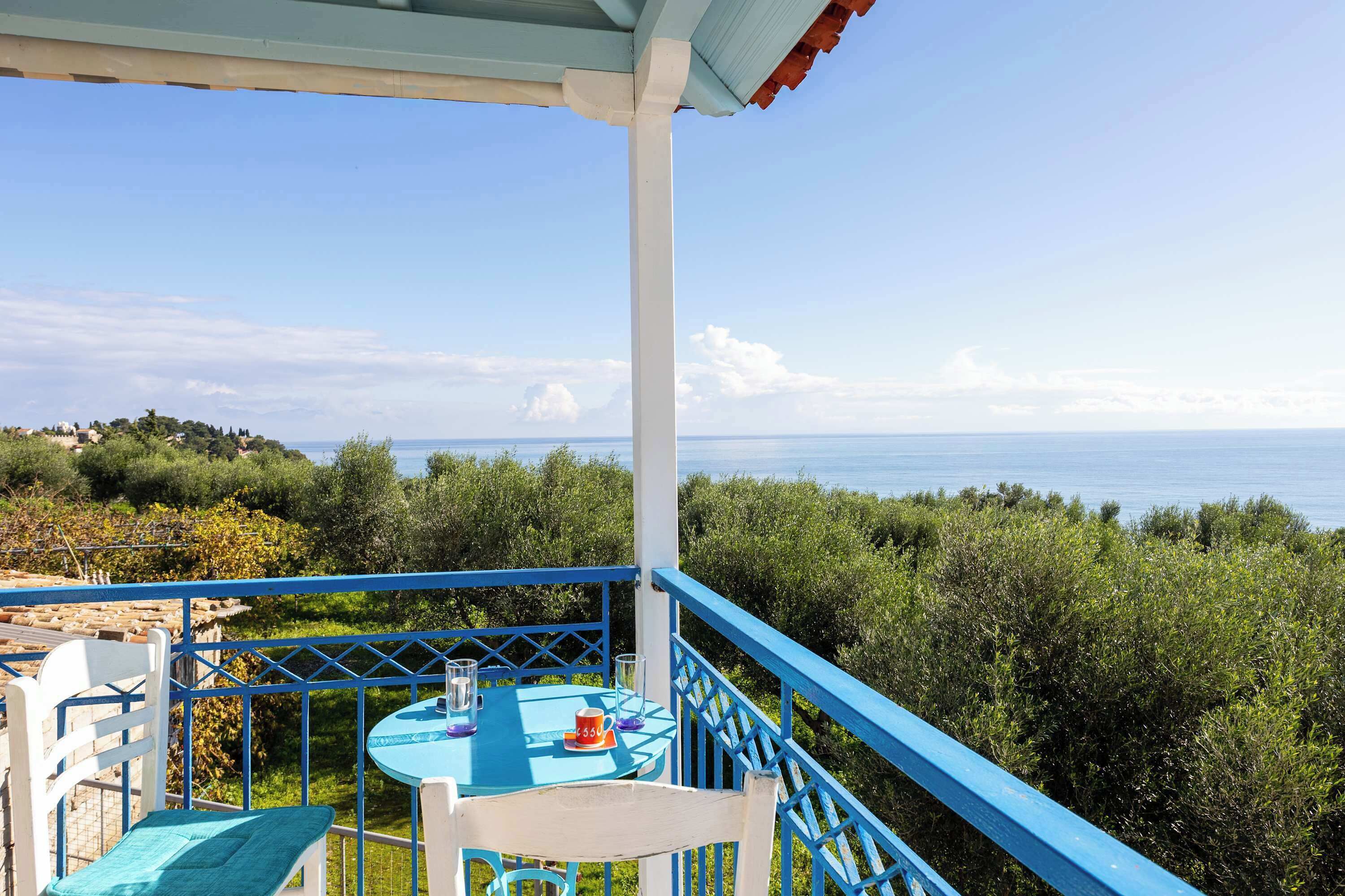 Un balcon avec une table et des chaises, donnant sur un paysage côtier avec des arbres et la mer.