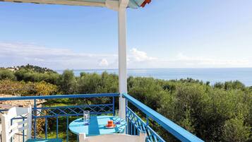 Un balcon avec une table et des chaises, donnant sur un paysage côtier avec des arbres et la mer.