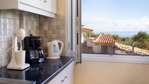 Una cocina con cafetera, hervidor y ventana con vistas a un tejado de tejas y árboles.