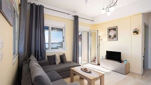 Una sala de estar con sofá, mesa de centro, televisor y vista al exterior.